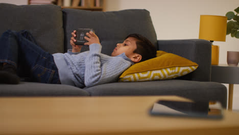Young-Boy-Lying-On-Sofa-At-Home-Playing-Game-Or-Streaming-Onto-Handheld-Gaming-Device-8